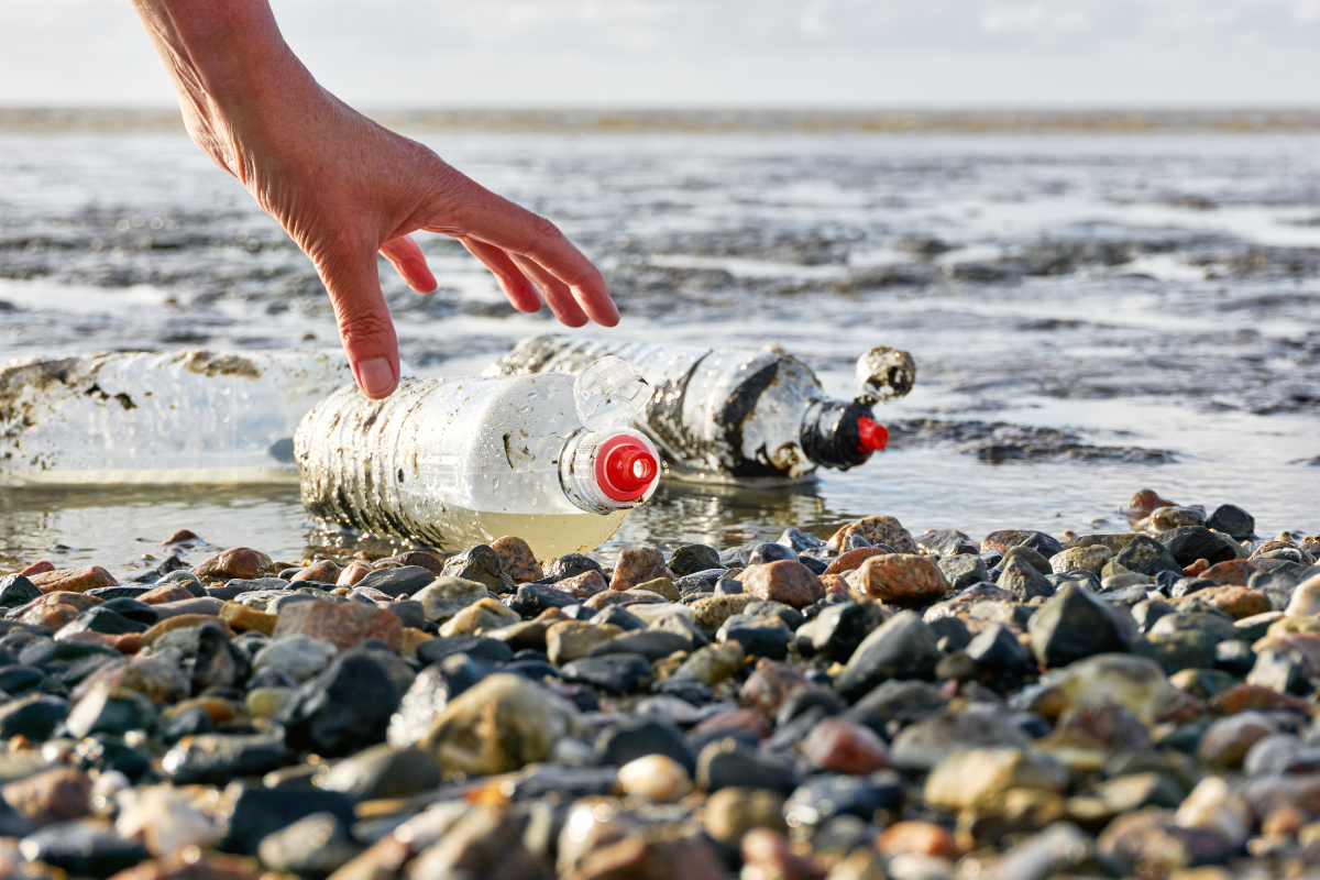 Plastic soep! Iemand raapt 2 gore flesjes op uit het water die aangespoeld zijn.